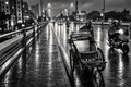 Moody black and white photography of cyclo driver pushing rickshaw across wet bridge on rainy night in Vietnam wall art print